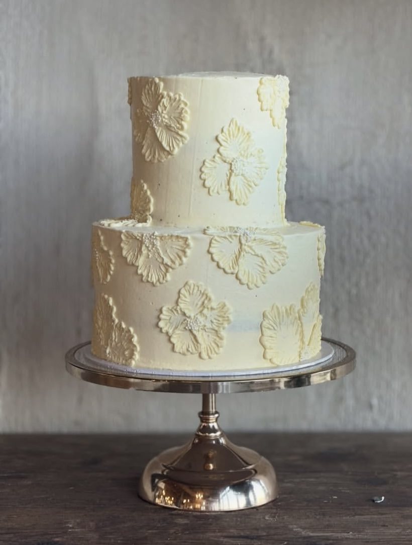 A two tier buttercream wedding cake with piped blossoms on a gold stand
