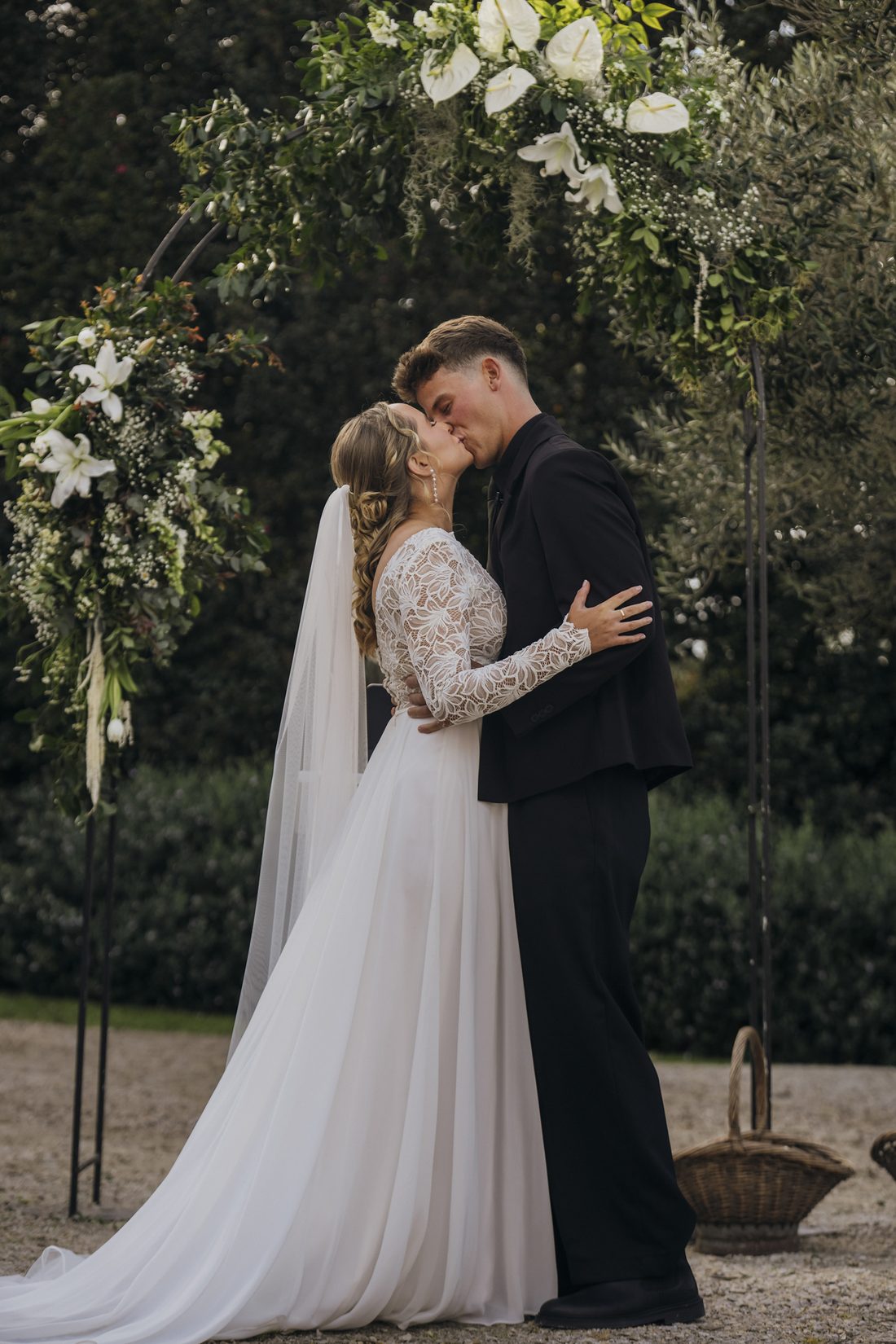 A couple sharing their first kiss beneath the floral arch