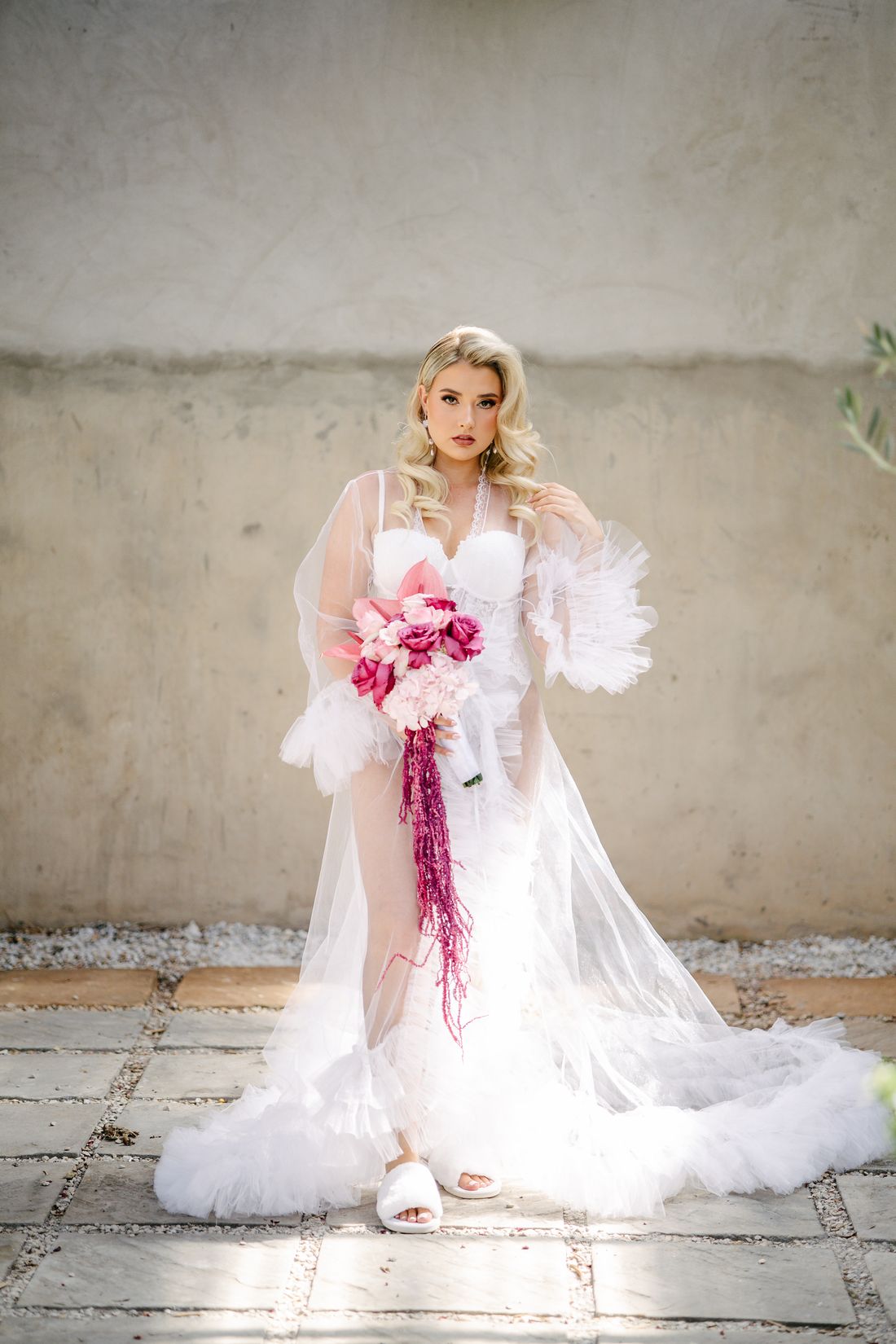 A bride in her robe with a pink bouquet on the morning of her wedding