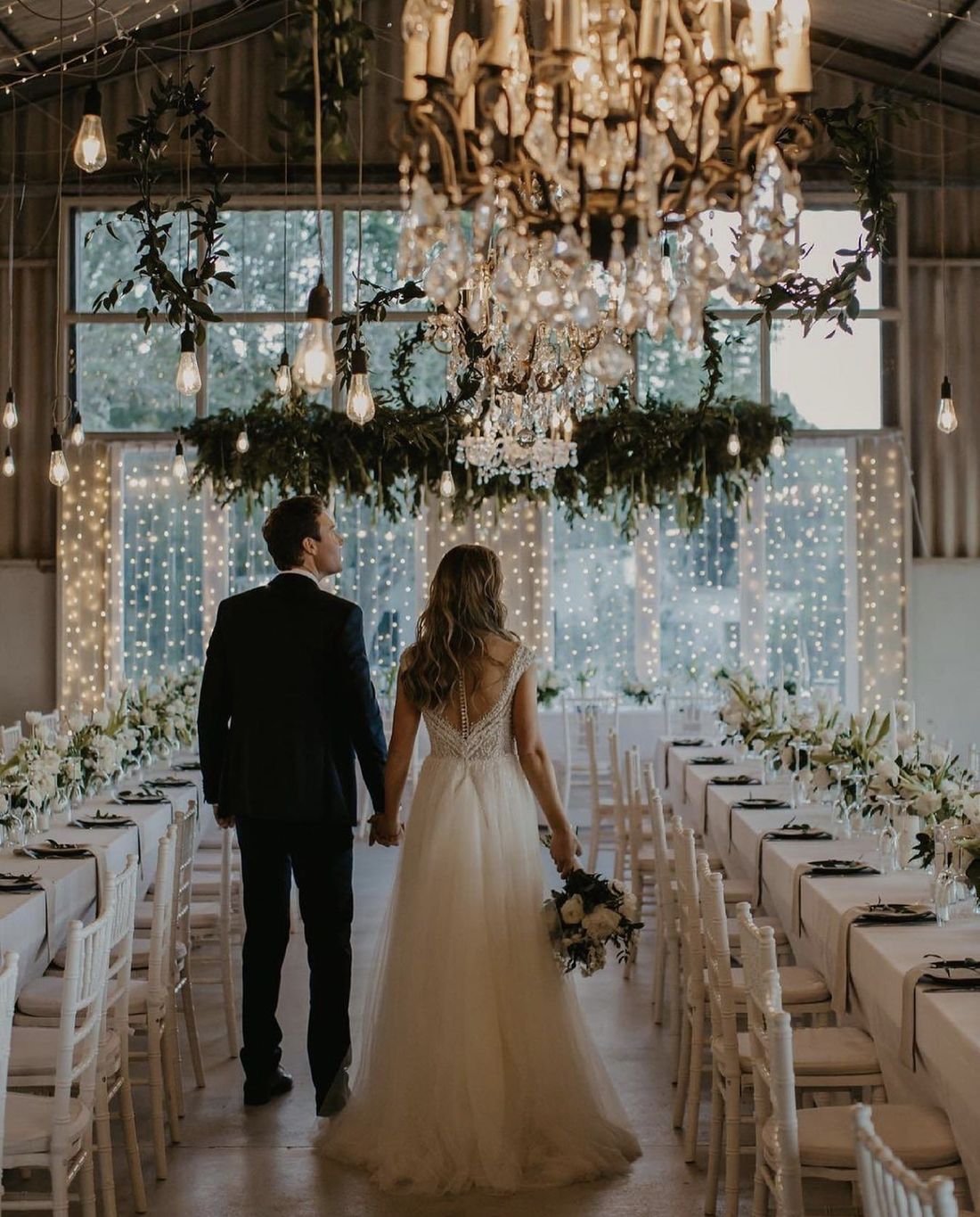 A couple walking into the reception beneath crystal chandeliers