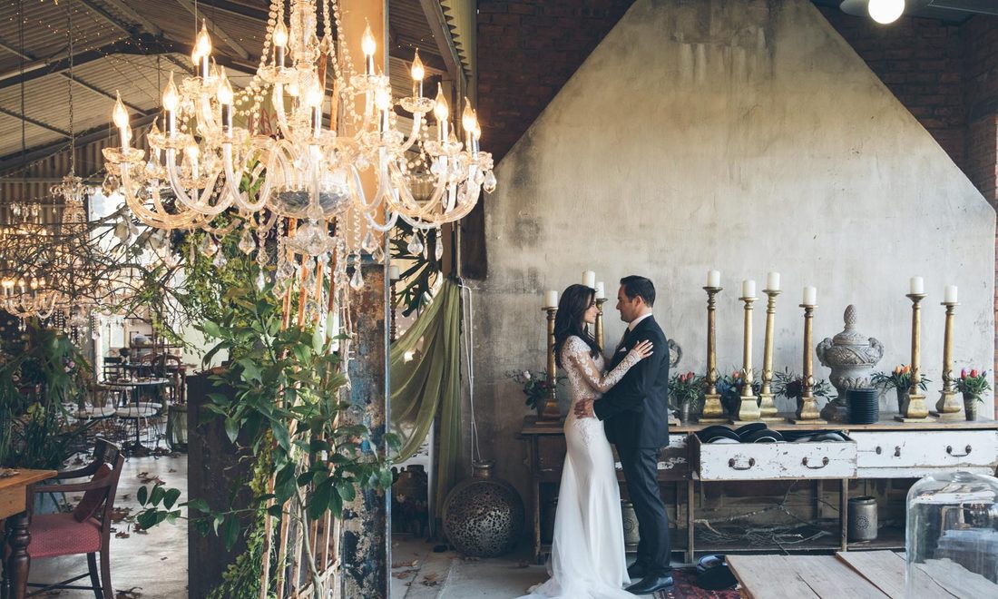 A bride and groom beneath crystal chandeliers in the barn