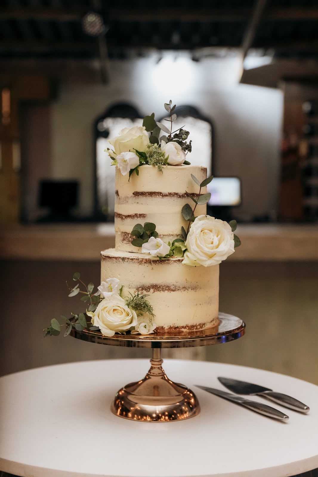 A semi naked wedding cake dressed with white roses and eucalyptus