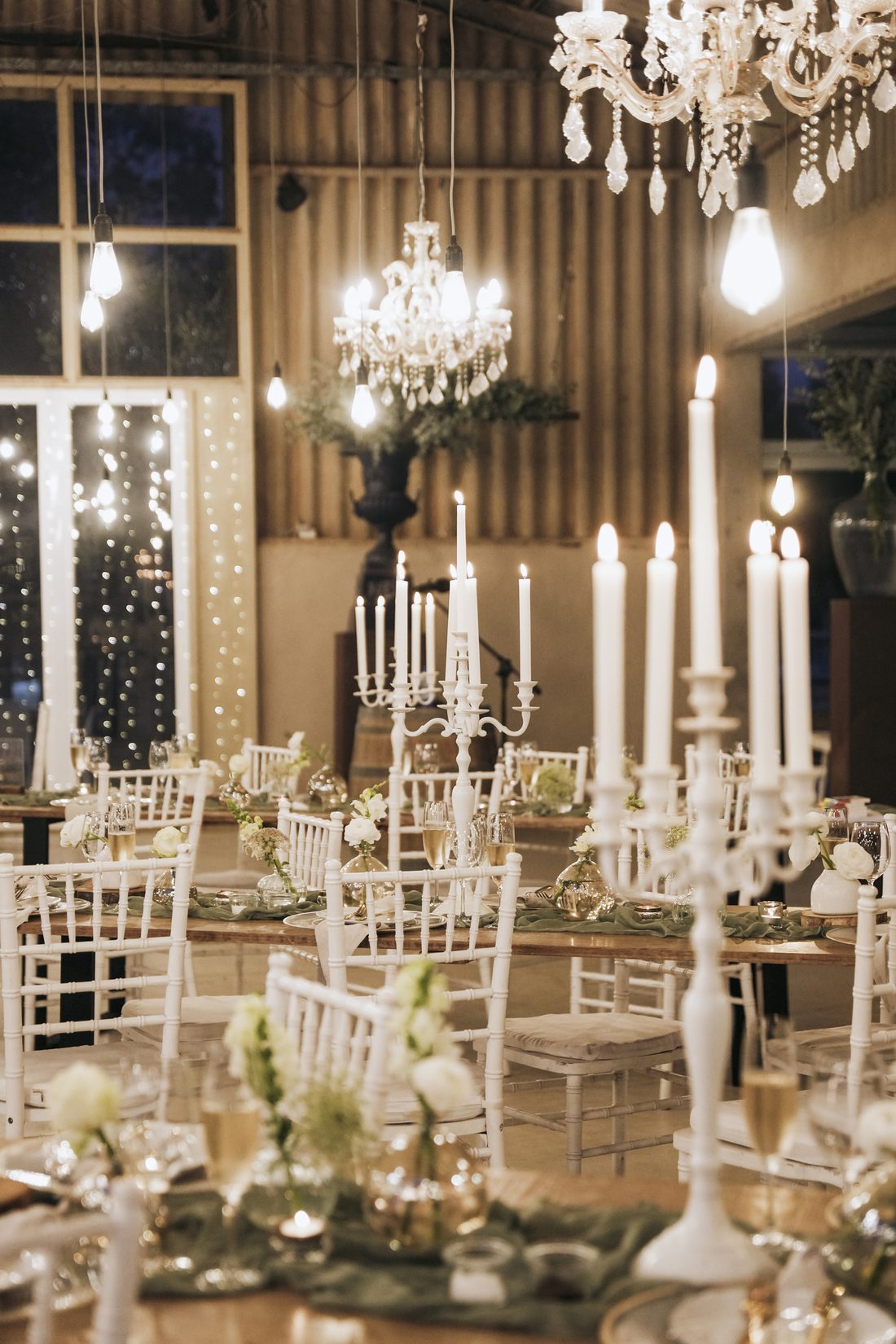 Candlelit tables set beneath crystal chandeliers in the barn